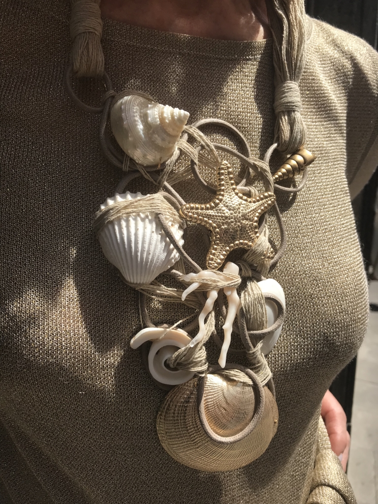 Dettaglio della collana indossata da Cilla. Splendida collana interamente realizzata e modellata a mano con filato in cotone cerato, filato di lino, elementi marini in plexiglas metallizzato dorato e vere conchiglie naturali e in madreperla. Un capolavoro di raffinata lavorazione artigianale di grande eleganza. E' un pezzo unico Haute Couture.