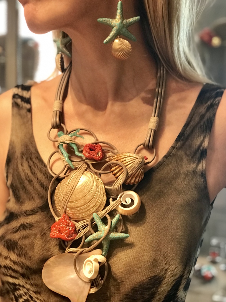 Una piccola scultura questa magnifica collana indossata da Raffy, interamente modellata a mano con filato in cotone cerato naturale e filato di lino. Come una in una rete splendidi elementi a tema marino sono imprigionati tra le volute, con una sapiente e minuziosa lavorazione artigianale: Conchiglie naturali, elementi in plexiglas e corallo naturale si mixano per un effetto scenografico dei più raffinati. Orecchini con stella marina e conchiglia in parure. Questi gioielli sono tutti pezzi unici di Cillabijoux.