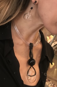 Molto particolare anche la parure indossata da Raffy. Collana realizzata a mano con rubber tube trasparente e ciondolo centrale, quest'ultimo realizzato con fettuccia in pelle, filato in cotone cerato, sfera in plexiglas nera ed elemento a ciambella in vetro. Orecchini con maxi boulle sempre in vetro. Sono tutti pezzi unici di Cillabijoux