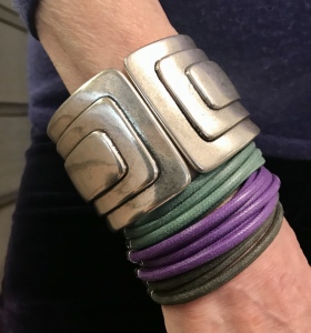 Cilla indossa due bellissimi bracciali: Uno a scatto, in plexiglas metallizzato argento, con motivi geometrici, essenziale e d'effetto. L'altro è un bracciale realizzato interamente a mano con fili di cotone cerato che formano fascia intorno al polso.