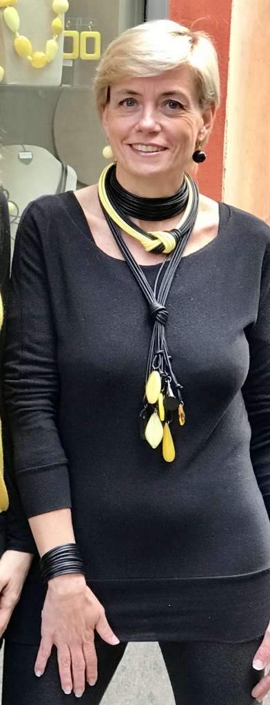 Sabrina indossa un "Collier de chain a fascia" ed un "Bracciale a fascia"  nella versione  01) Nero, insieme ad una "Collana a frusta con charms in plexiglas"  01/40) Nero/Giallo